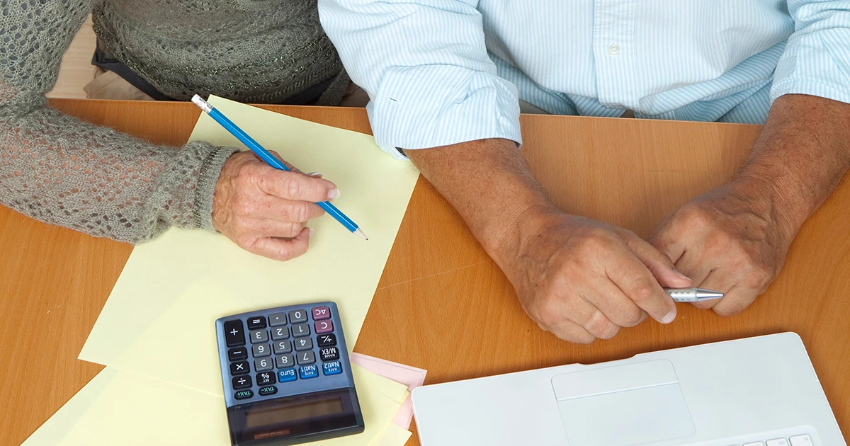 Retired couple reviewing household budget documents at a kitchen table with a calculator and coffee